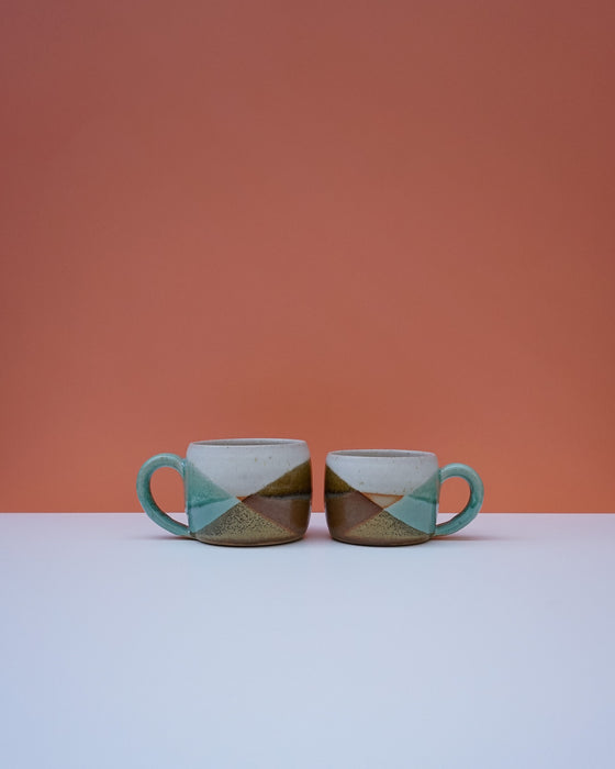 Two ceramic mugs with geometric pattern on a white surface and orange background. Liz Vidal Ceramics | Shop Fodder