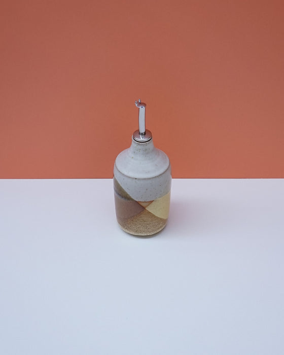 Ceramic bottle with a striped design on a white surface and orange background. Liz Vidal Ceramics | Shop Fodder