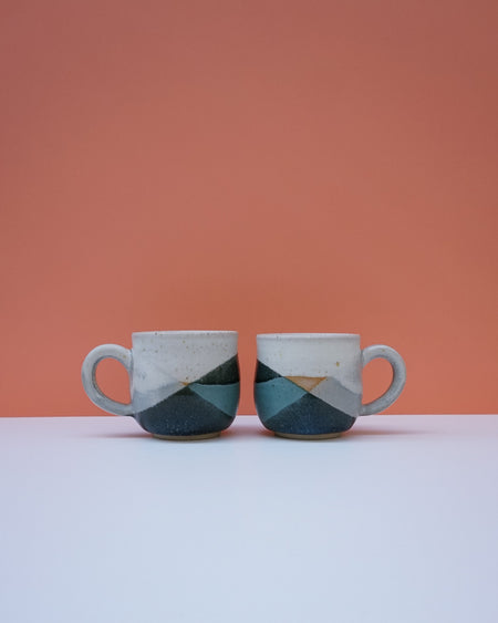 Two ceramic mugs with geometric design on a white surface and peach background. Liz Vidal Ceramics | Shop Fodder