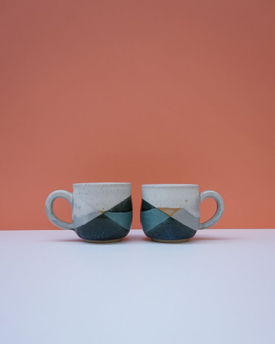 Two ceramic mugs with geometric design on a white surface and peach background. Liz Vidal Ceramics | Shop Fodder