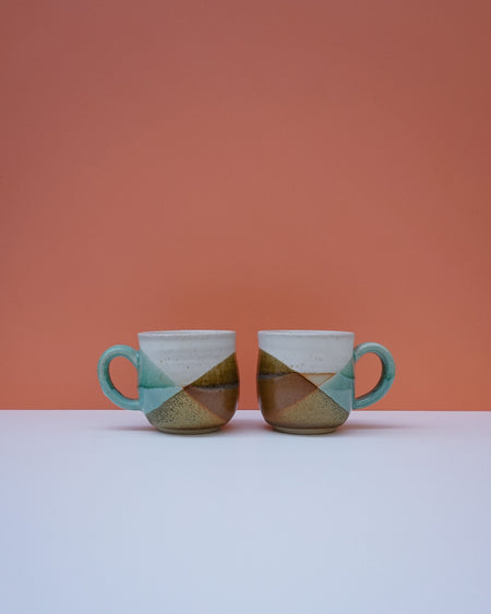 Two ceramic mugs with a geometric design on a white surface and orange background. Liz Vidal Ceramics | Shop Fodder