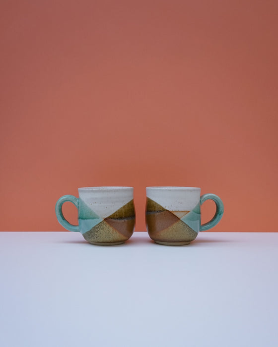Two ceramic mugs with a geometric design on a white surface and orange background. Liz Vidal Ceramics | Shop Fodder