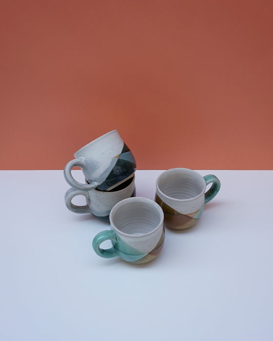 Three ceramic cups with green handles on a white surface against an orange background. Liz Vidal Ceramics | Shop Fodder