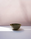 A small handmade ceramic bowl with a textured olive-green glaze sits on a white surface against a soft pink background. Morning Bowl | Scree Ceramics | Fodder
