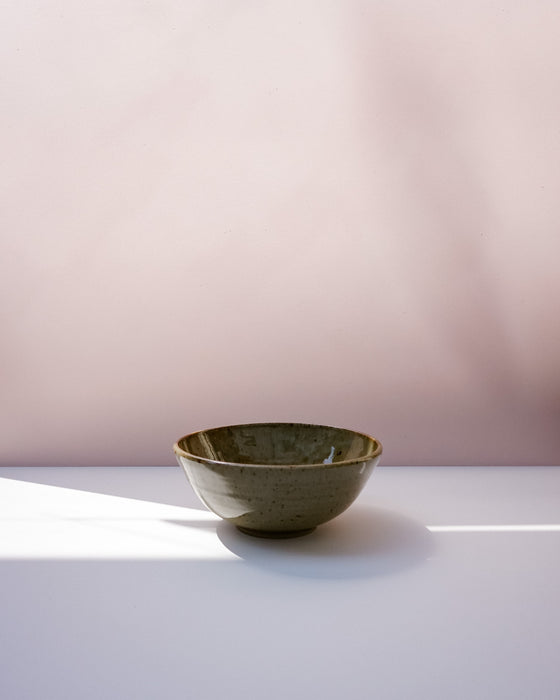 A small handmade ceramic bowl with a textured olive-green glaze sits on a white surface against a soft pink background. Morning Bowl | Scree Ceramics | Fodder