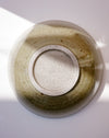An overhead close-up of a round ceramic bowl with a speckled sage green and beige glaze, photographed on a white surface with soft natural shadows. Morning Bowl | Scree Ceramics | Fodder