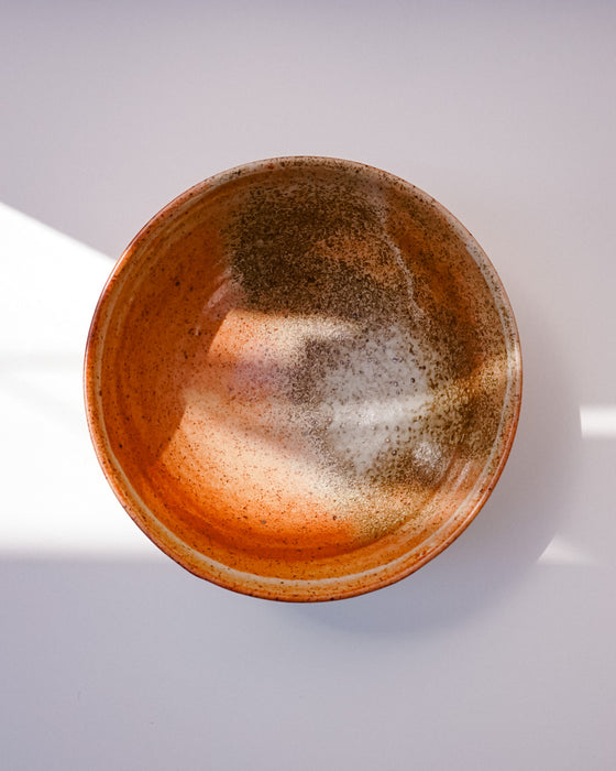 A handmade ceramic bowl with a textured, speckled glaze in earthy brown, orange, and beige tones, photographed from a top-down perspective on a light gray background. Morning Bowl | Scree Ceramics | Fodder