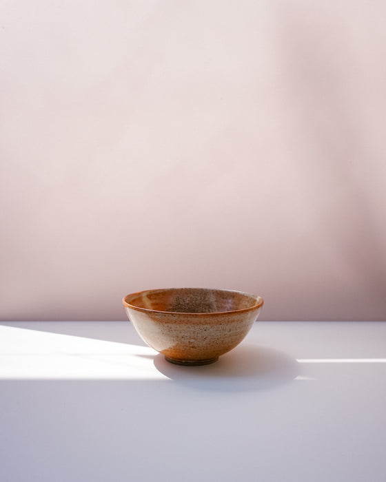 A small handmade ceramic bowl with a speckled brown and beige glaze, sitting on a white surface with soft shadows against a pale pink background. Morning Bowl | Scree Ceramics | Fodder