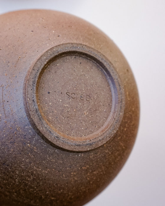 Close-up of the bottom of a brown ceramic vessel, showing a textured stoneware surface and a stamped maker's mark reading 'SCREE' on a light gray background. Morning Bowl | Scree Ceramics | Fodder