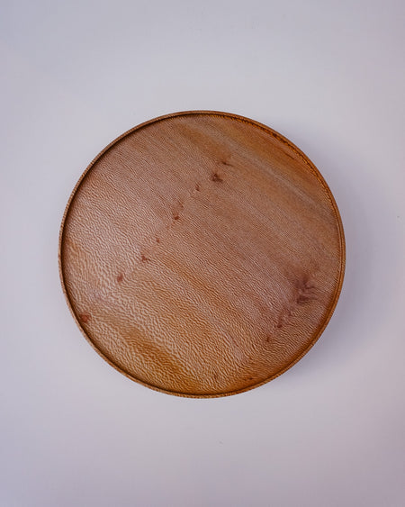 A round wooden tray with a textured pebbled leather-like finish, photographed from directly above on a plain light background. London Plane wooden cake stand by Selwyn House - lacewood grain - Fodder