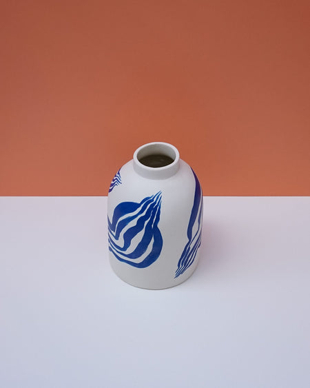 White vase with blue patterns on a white surface and orange background. Sophie Alda | Handmade Ceramics | Shop Fodder