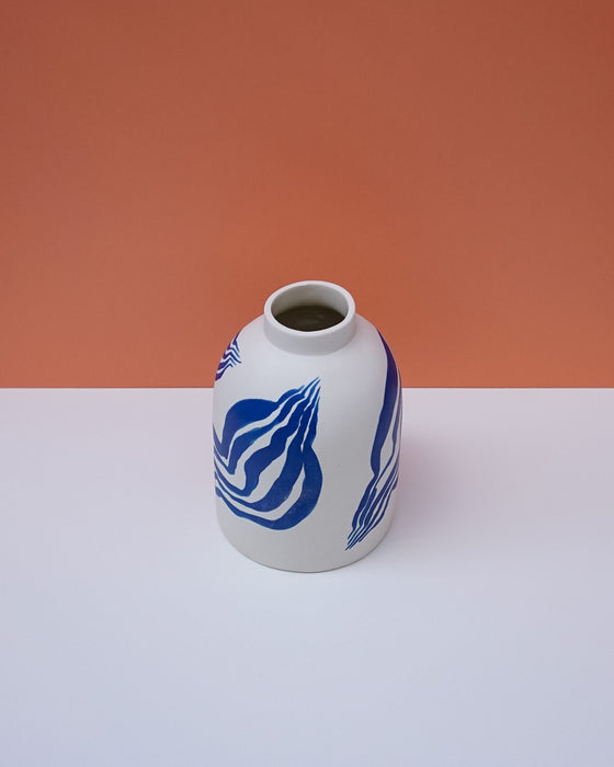 White vase with blue patterns on a white surface and orange background. Sophie Alda | Handmade Ceramics | Shop Fodder