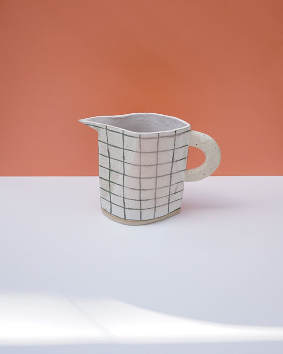 Ceramic pitcher with grid pattern on a white surface and peach background. Sophie Alda | Handmade Ceramics | Shop Fodder