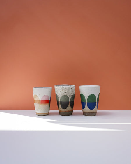 Three ceramic cups with colorful patterns on a white surface and orange background. Sophie Alda | Handmade Ceramics | Shop Fodder
