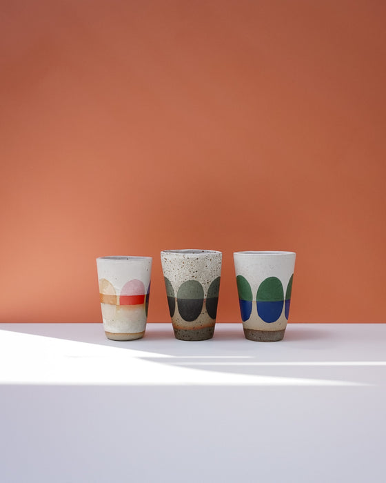 Three ceramic cups with colorful patterns on a white surface and orange background. Sophie Alda | Handmade Ceramics | Shop Fodder
