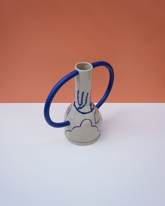 Ceramic vase with blue handles on a white surface against an orange background. Sophie Alda | Handmade Ceramics | Shop Fodder