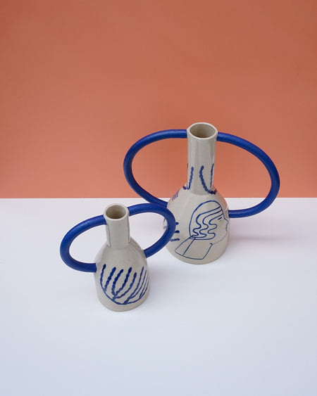 Two ceramic vases with blue handles on a white surface against an orange background. Sophie Alda | Handmade Ceramics | Shop Fodder