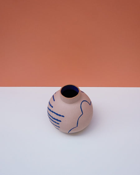 Ceramic vase with blue abstract patterns on a white surface with a peach-colored background. Sophie Alda | Handmade Ceramics | Shop Fodder