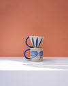 Ceramic mug with blue floral design and a matching funnel on a peach background. Sophie Alda | Handmade Ceramics | Shop Fodder