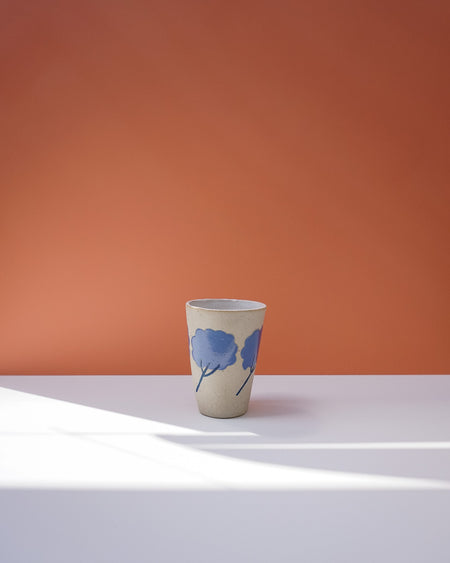 Ceramic cup with blue floral design on a white surface with an orange background. Sophie Alda | Handmade Ceramics | Shop Fodder