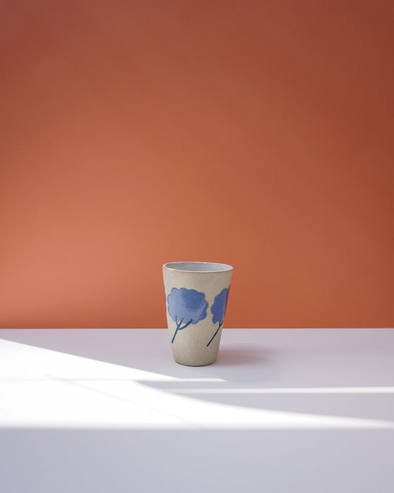 Ceramic cup with blue floral design on a white surface with an orange background. Sophie Alda | Handmade Ceramics | Shop Fodder