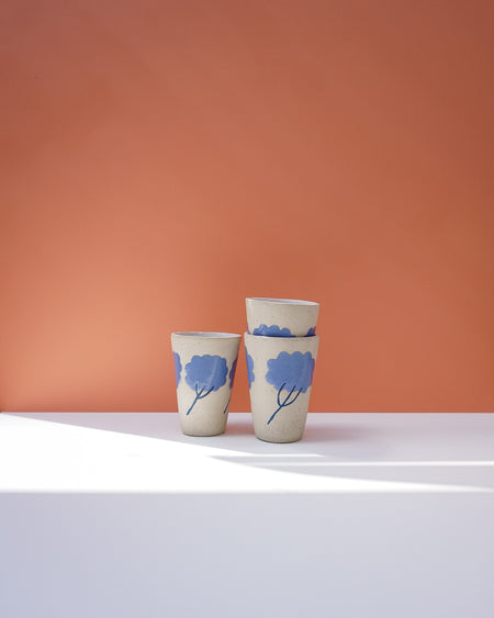 Three ceramic cups with blue floral designs on a peach background. Sophie Alda | Handmade Ceramics | Shop Fodder