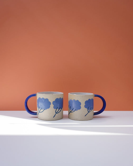 Two ceramic mugs with blue floral designs on a white surface and orange background. Sophie Alda | Handmade Ceramics | Shop Fodder