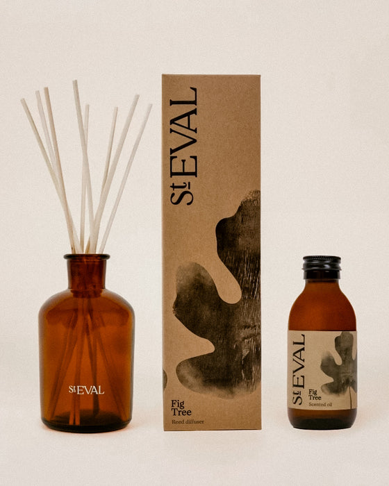 Seval Fig Tree scented oil diffuser set including an amber glass reed diffuser bottle with reeds, a tall brown kraft paper box, and a smaller amber glass bottle with a black cap, all on a warm beige background. Fig Tree reed diffuser by St Eval - fresh green home fragrance - Fodder