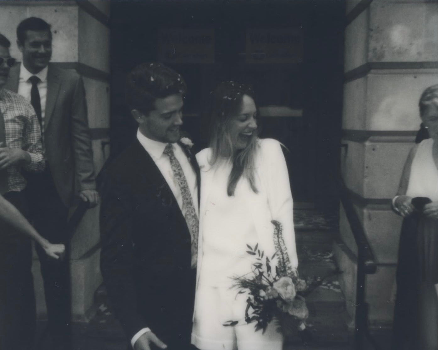 Black and white photo of a couple outside Camden Town Hall on their wedding day with guests in the background. | Unique Gift List | Fodder