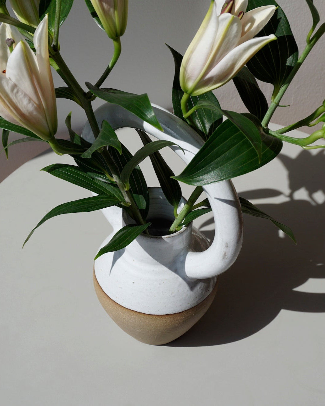 Lily Pearmain Ceramics | Doughnut Vase | Shop Fodder. A bellied vase with an oversized round handle at the top. with a bunch of lillies. 