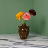 a dark brown hand made bud vase with three flowers. 