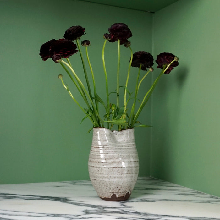 deep red flowers in an handmade ceramic vase on a marble table with a green background. 