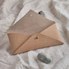 sand coloured leather envelope thats open on a cloth background. with a stone in the foreground. 