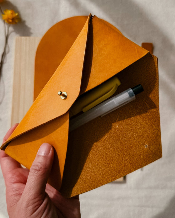Hand holding a brown leather pouch with stationery items on a neutral background
