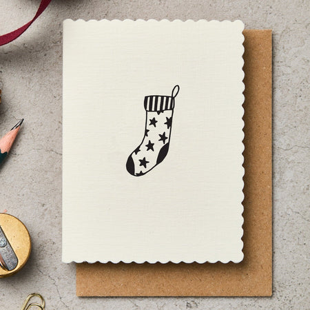Greeting card with a Christmas stocking design, pen, and decorative items on a textured surface