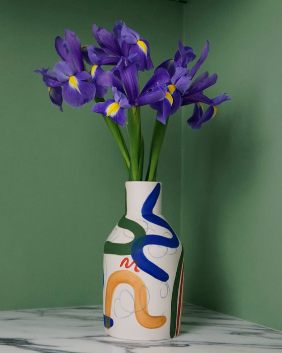 porcelain vase with abstract brushwork pattern and a bunch of iris flowers on a green background. 