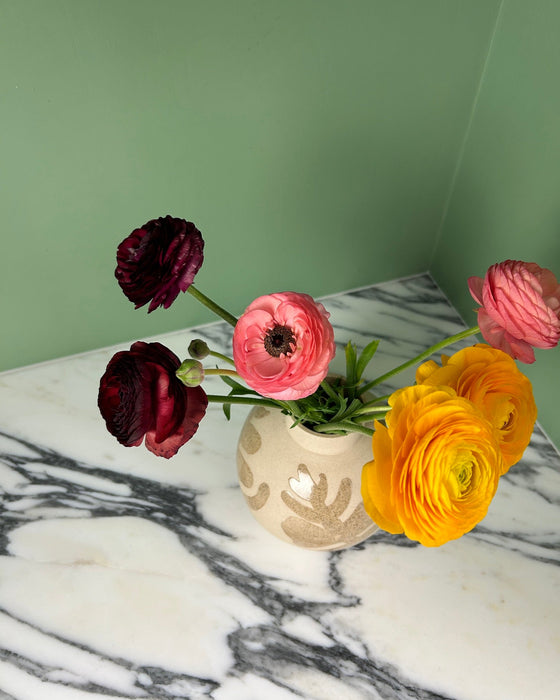 Vase with pink, red, and yellow flowers on a marble surface against a green wall. Sophie Alda | Handmade Ceramics | Shop Fodder