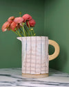 handmade jug with yellow handle and a bunch of pink flowers on a marble table with a green background. Sophie Alda | Handmade Ceramics | Shop Fodder