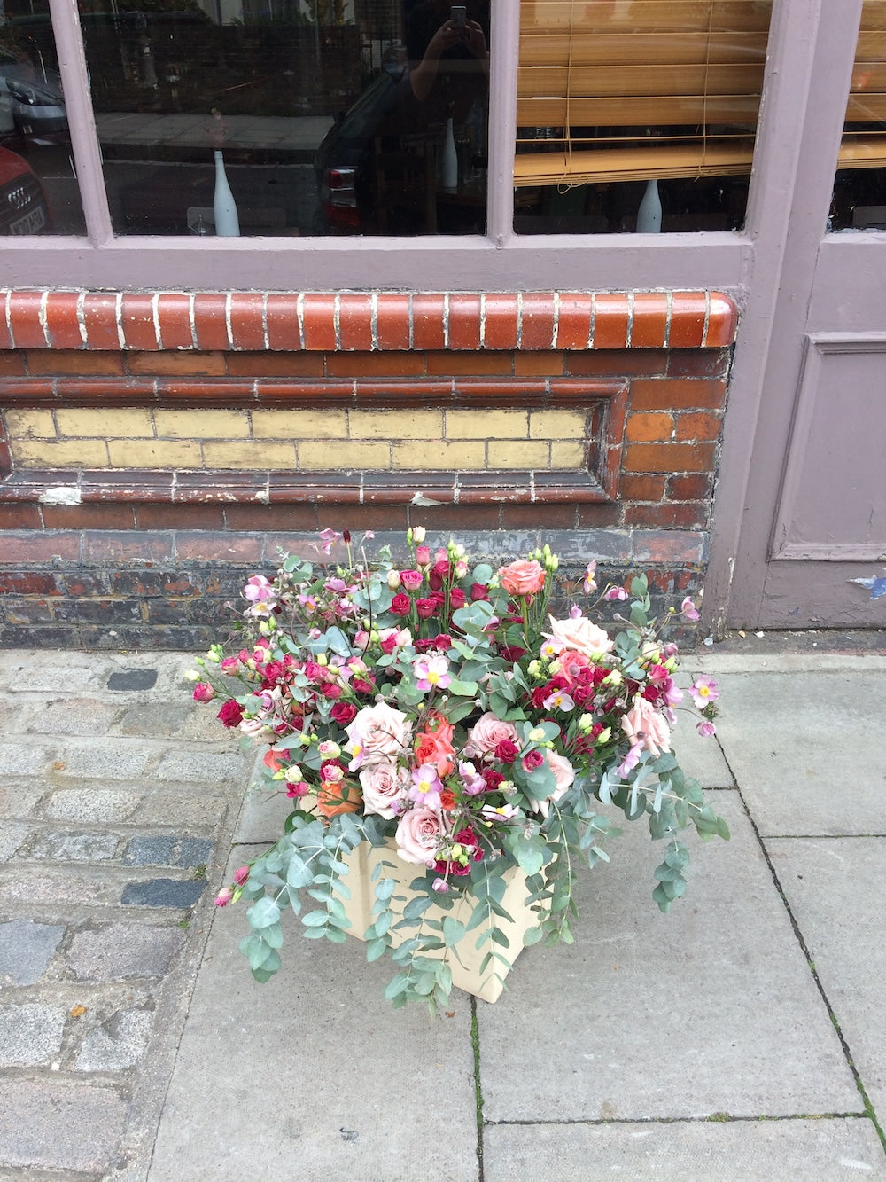 Floral arrangement on a sidewalk in front of a building entrance - Brian & Margaret Wedding Flowers - Highgate | Bespoke Wedding list | handmade Ceramics | Fodder