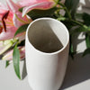 detail of the neck of a white ceramic vase with a bunch of lilies sitting next to the vase. 