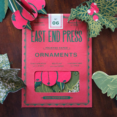 Box of East End Press ornaments with decorative paper holly leaves and berries on a wooden surface. East End Press | Shop Fodder